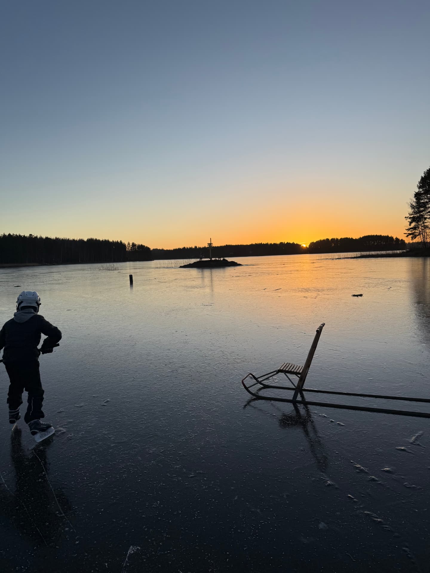 Lapsi luistelemassa järven jäällä auringonlaskussa